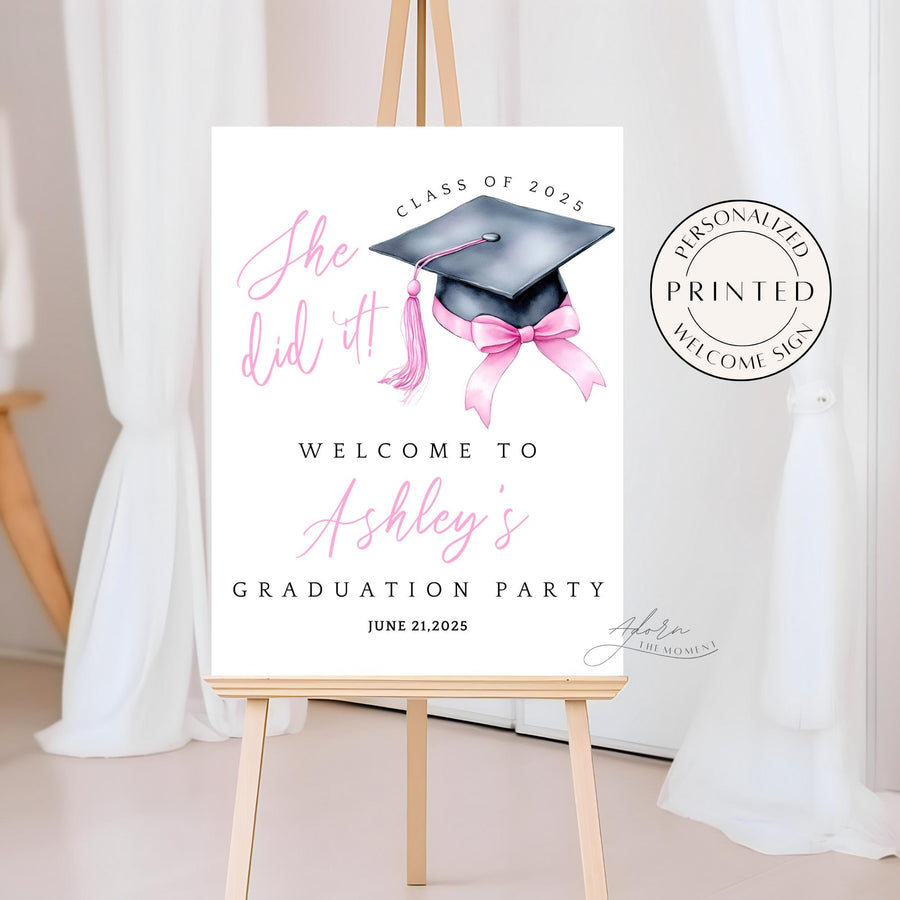 A printed She Did It! graduation welcome sign featuring a black graduation cap, a pink tassel, and a pink coquette bow. This high-quality printed sign is perfect for decorating a high school or college graduation party.