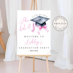 A printed She Did It! graduation welcome sign featuring a black graduation cap, a pink tassel, and a pink coquette bow. This high-quality printed sign is perfect for decorating a high school or college graduation party.